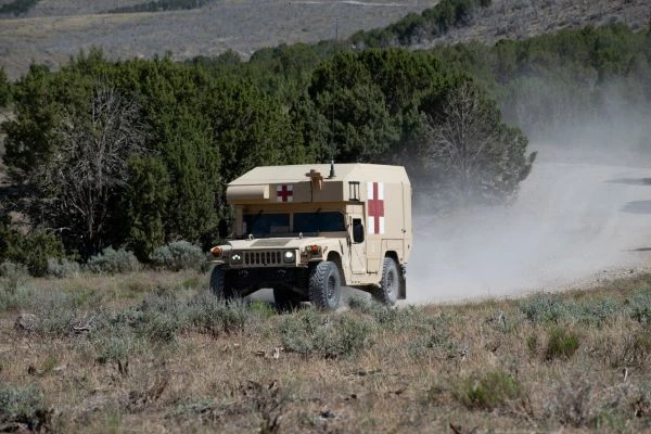 A military ambulance drives down a dusty road