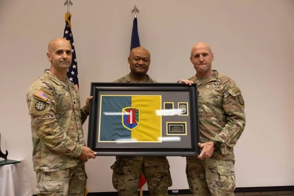 Three uniformed soldiers pose for a photo with a framed flag