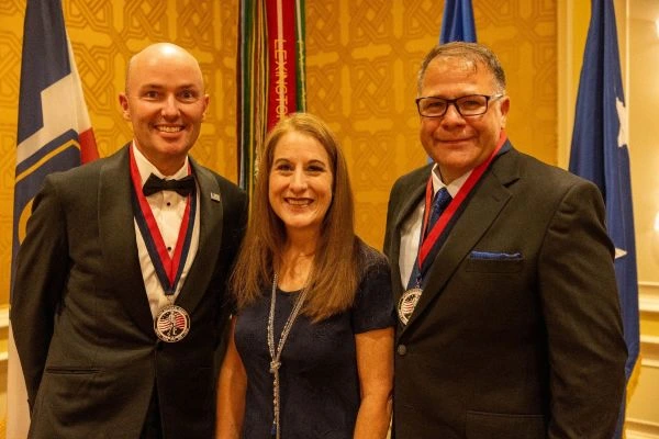 Two men and a woman pose at a formal event