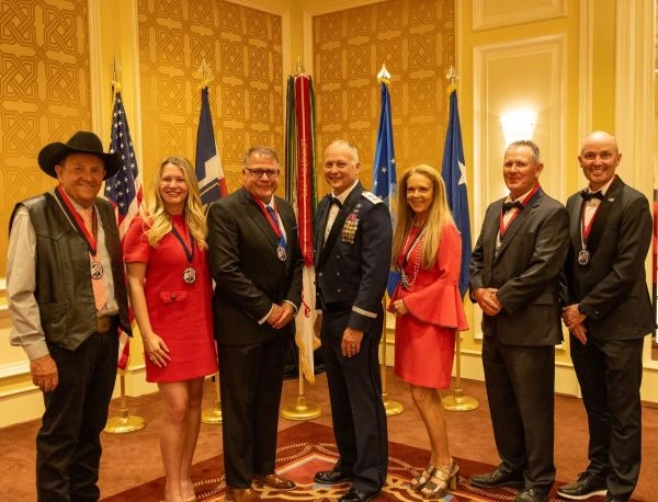 A group of people, including a man in uniform pose in front of flags
