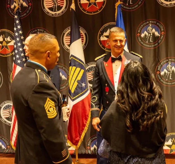 A decorated servicemember greets another servicemember and his wife