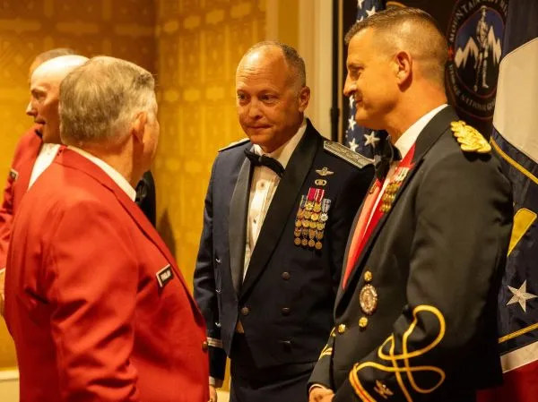 Two decorated servicemembers greet a man at a formal event