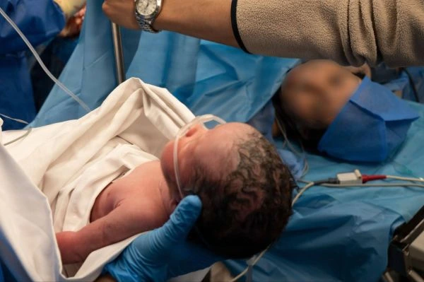 A newborn infant is held by a caretaker with blue surgical gloves