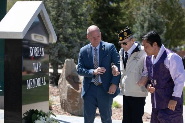 Two men escort an elderly military veteran to see a military monument