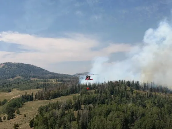 A helicopter flies in a smoky canyon carrying a bucket of water