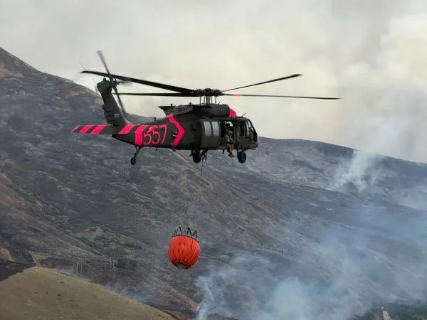 A helicopter flies in a smoky canyon carrying a bucket of water