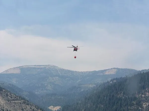 A helicopter flies in a smoky canyon carrying a bucket of water