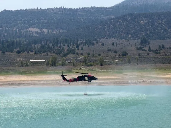 A helicopter filling a bucket of water from a reservoir