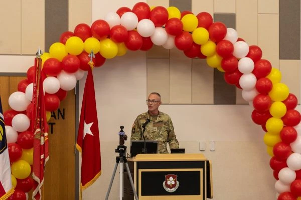 US Army Utah National Guard officer speaking at a podium framed by a red, white, and yellow balloon arch and military flags.