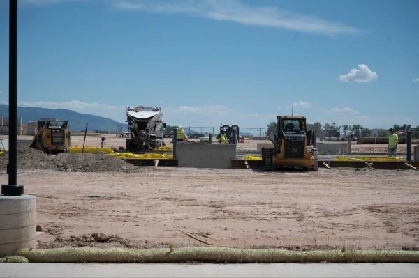 Construction site with a concrete mixer, front loaders, and workers preparing a foundation under a clear sky.