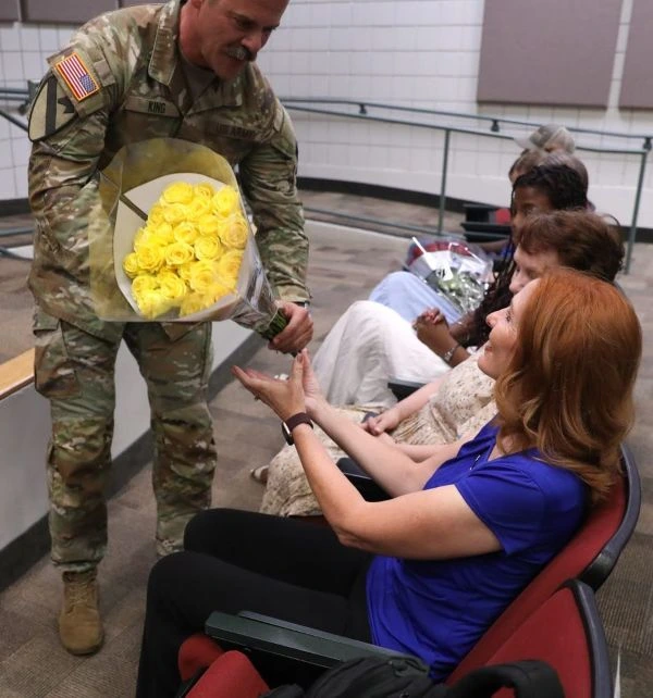 A uniformed servicemember presents flowers to a woman in a blue blouse
