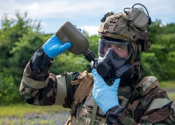 An airman in full MOPP chemical protective gear and a gas mask drinks water from a canteen using an attached drinking tube
