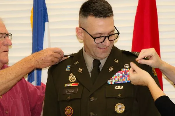 Close-up view of family members attaching one-star general officer rank insignia onto the epaulets of a smiling U.S. Army officer's uniform.