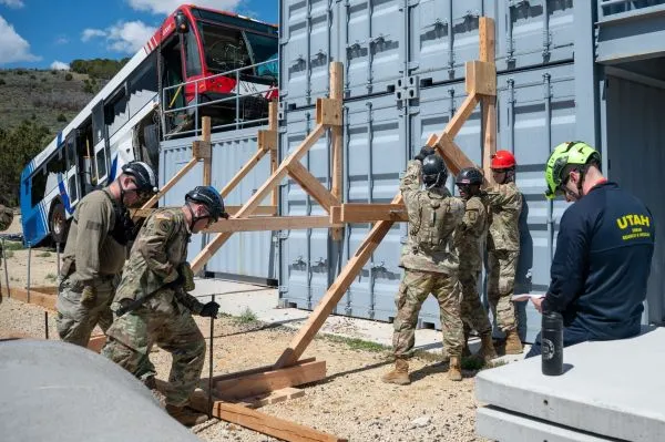 Servicemembers build a wood framed platform next to shipping containers in a training village