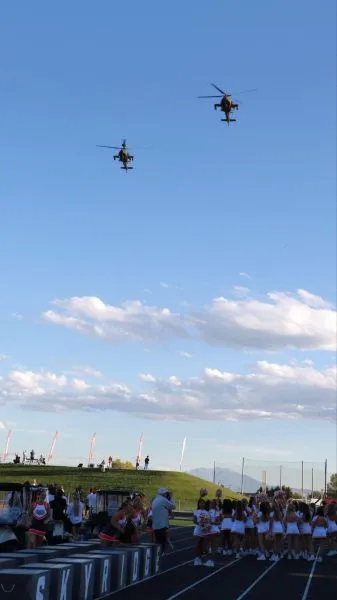 Two helicopters flying above a sports field