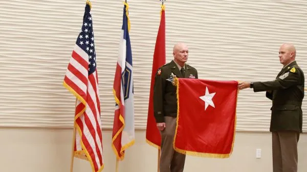 A senior enlisted leader presenting a red one-star general officer flag to Brig. Gen. Shawn M. Fuellenbach