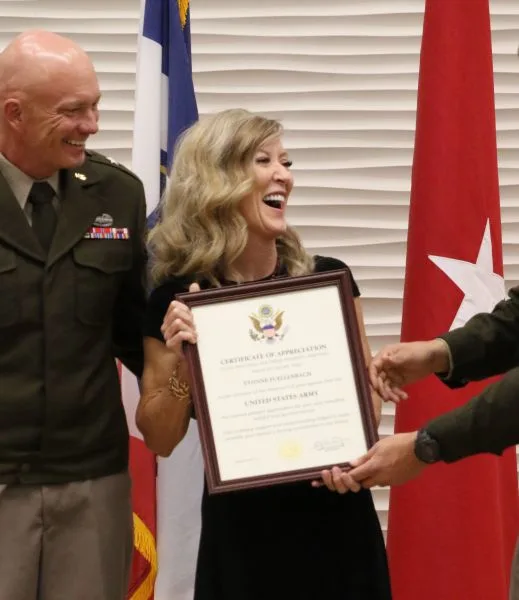 The wife of Brig. Gen. Shawn M. Fuellenbach smiling while holding a framed Certificate of Appreciation