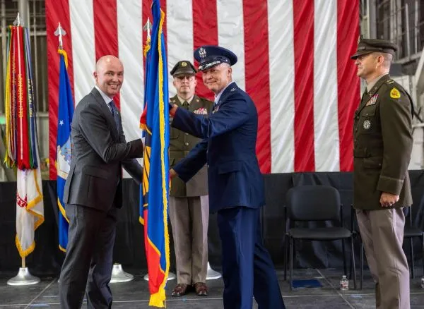 An official passes an organizational guidon flag to a military officer on stage.