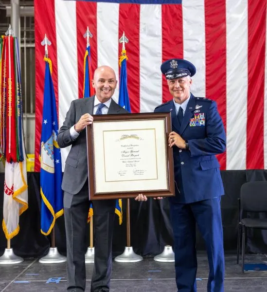An official and an Air Force officer hold up a framed state certificate of recognition.