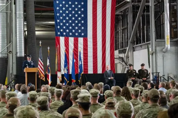 An Air Force officer addresses a crowd from a podium inside an aircraft hangar.