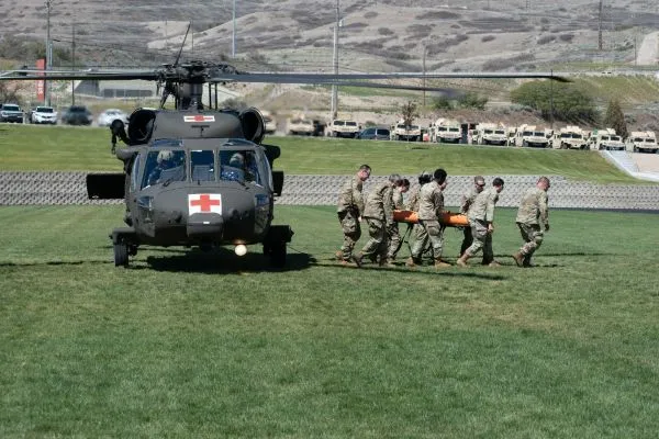 Servicemembers carry a medical training mannequin out of a helicopter