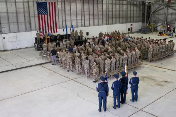 High-angle wide view of Utah Air National Guard service members seated and standing in formation during a ceremony inside an airfield hangar