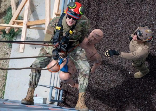 An airman practices ropes rescue with a mannequin as a second Soldier stands by