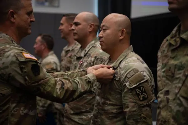 A U.S. Army officer pinning a badge onto the uniform collar of a soldier standing in line during a military ceremony