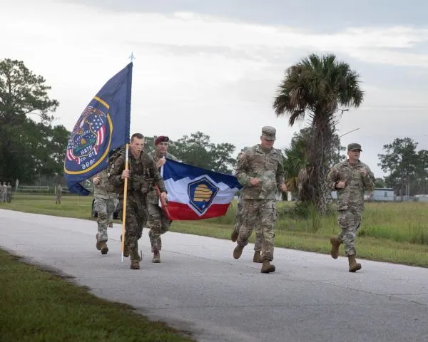 Multiple men in uniform run with the Utah state flags
