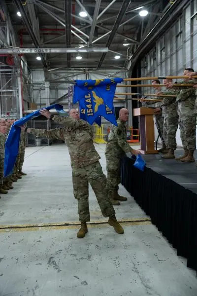Airmen in camouflage uniforms casing unit flags into blue sheaths during a Utah Air National Guard redesignation ceremony in an aircraft hangar