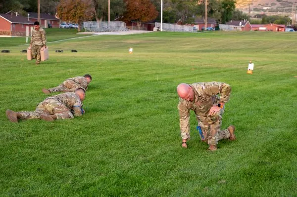 Soldiers performing low crawls and water can carries on a lawn during physical training