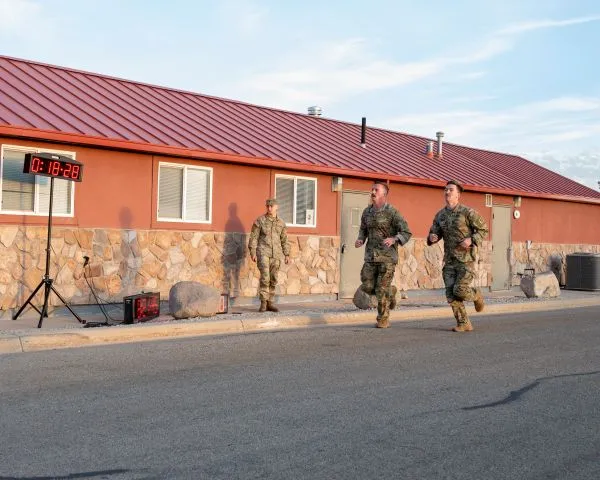 Two Soldiers running past a digital timer clock during a physical fitness run