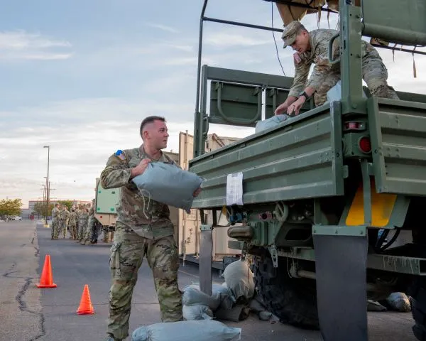 Soldier loading heavy sandbags into the back of a military cargo truck during a physical test