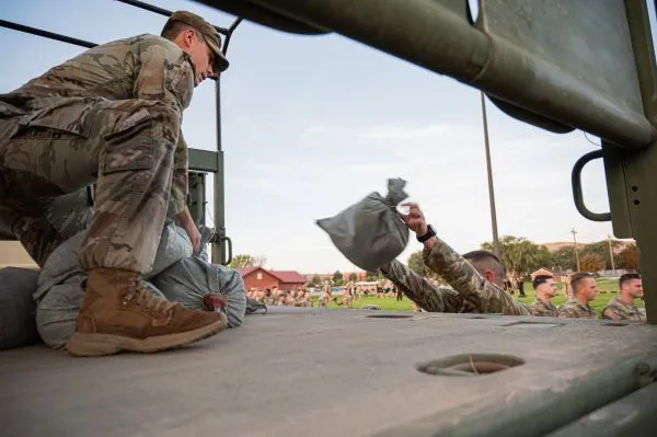 Soldier tossing a sandbag up to another Soldier positioned inside a military truck bed