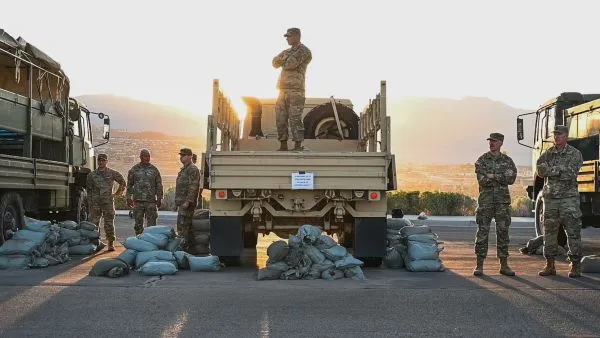 Soldiers standing by piles of sandbags next to military trucks during a physical fitness event